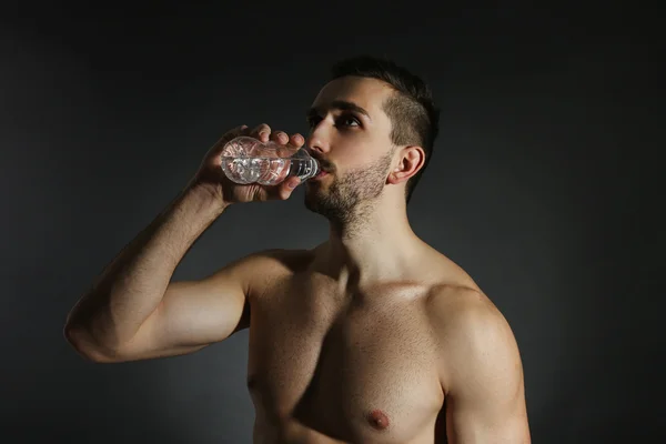 Muscle young man holding bottle of water on black background — Stock Photo, Image