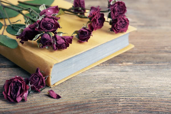Rosas secas com livro sobre mesa de madeira, close-up — Fotografia de Stock