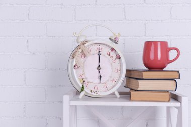Çalar saat, kitaplar ve pembe Kupası masa üzerinde beyaz tuğla yığını ile iç tasarım duvar arka plan