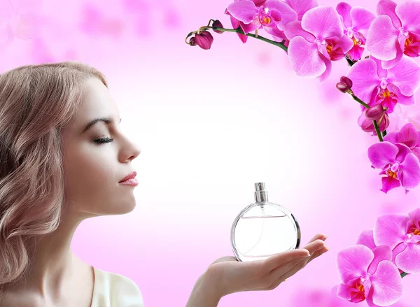 Красива жінка з пляшкою парфумів у квітах на рожевому фоні — стокове фото