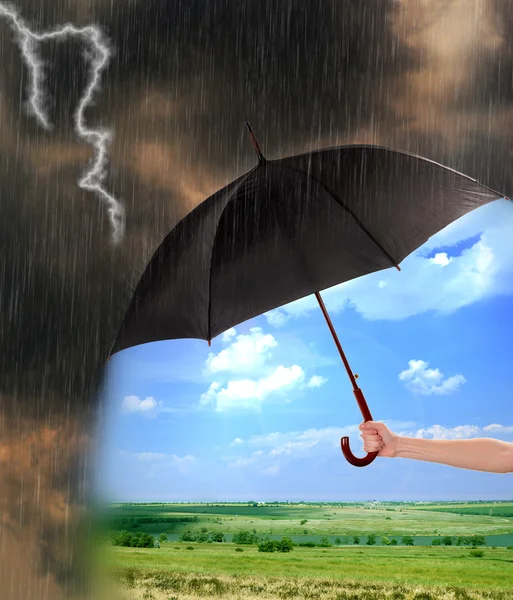 Schwarzer Regenschirm in der Hand schützt gutes Wetter vor dunklen Regenwolken — Stockfoto