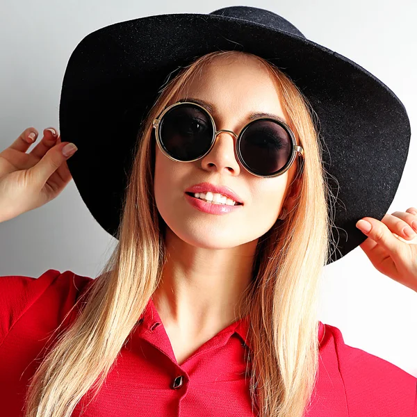 Portrett av ung modell i rød kjole, svart hatt og solbriller med grå bakgrunn – stockfoto