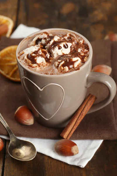 Cup of hot coffee with marshmallow on napkins with hazelnut, cinnamon and dried orange on rustic wooden planks background — Stock Photo, Image