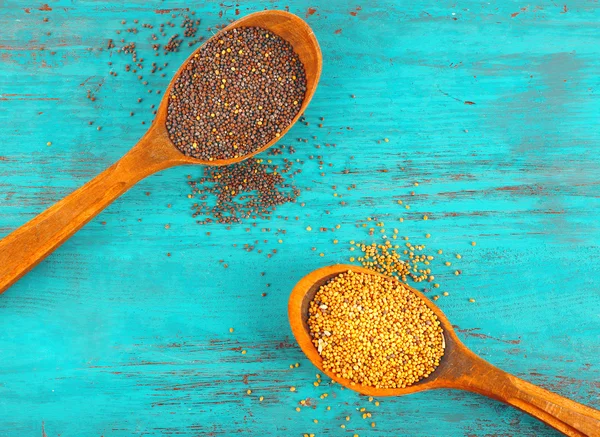 Dos tipos de semillas de mostaza en cuchara de madera sobre fondo de mesa de madera de color — Foto de Stock