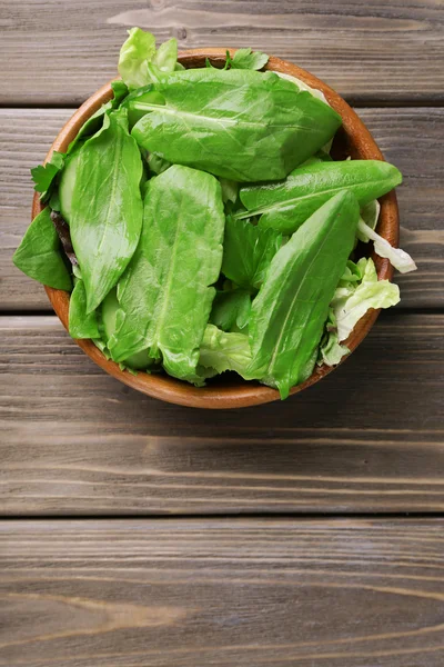 Mélange de feuilles de salade dans un bol sur des planches de bois — Photo