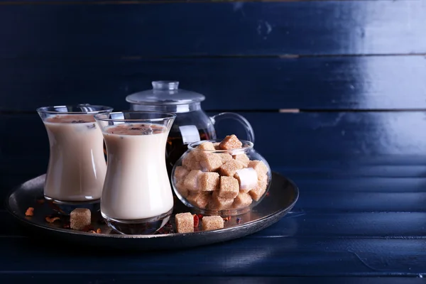 Black tea with milk in glasses and teapot with lump sugar on metal tray and color wooden planks background — Stock Photo, Image