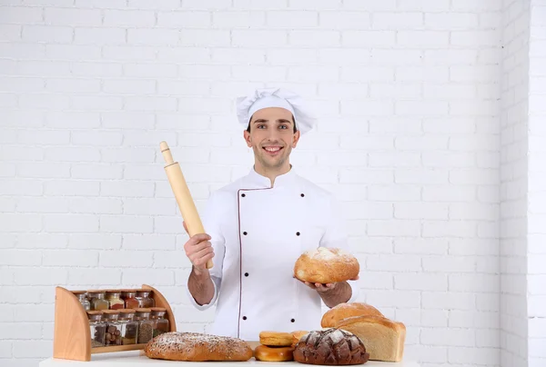 Baker in kitchen at table with freshly loaves of bread on white brick wall background — Stock Photo, Image