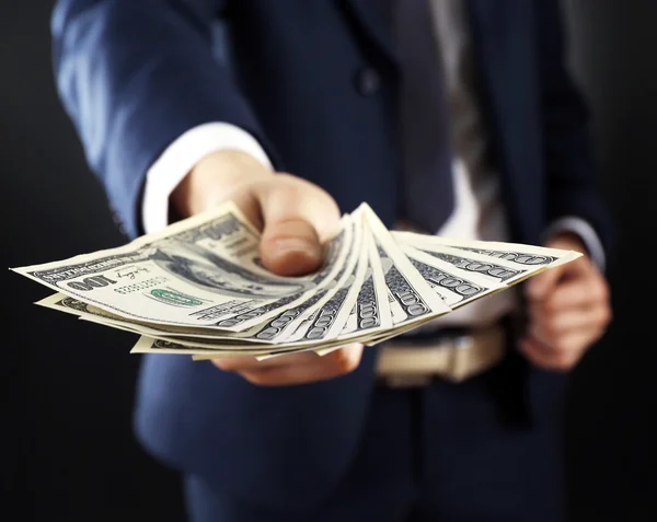 Businessman giving money on dark background — Stock Photo, Image