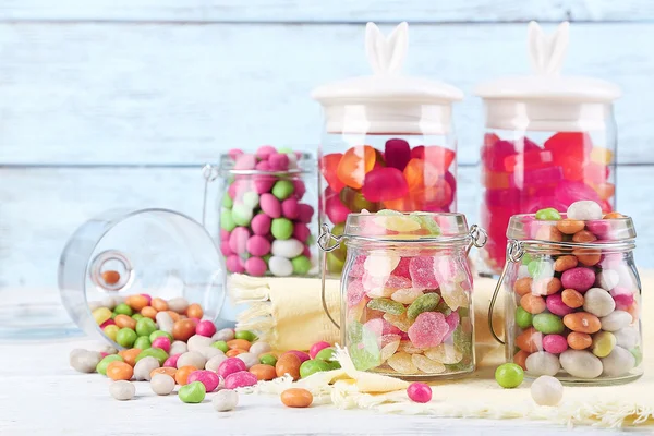 Multicolor snoepjes in glazen potten op een houten achtergrond kleur — Stockfoto