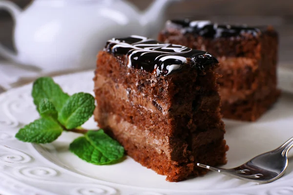 Вкусные кусочки шоколадного торта с мятой на фоне деревянного стола — стоковое фото