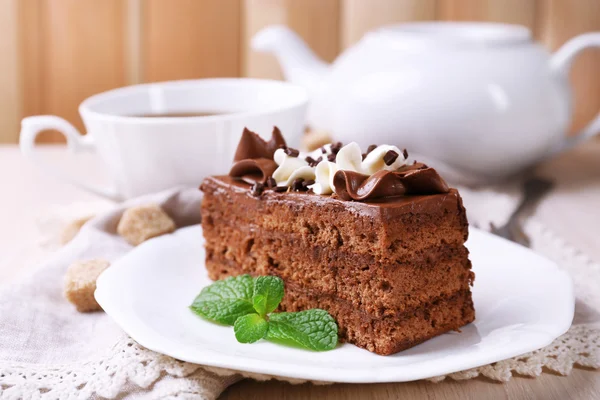 Вкусный кусок шоколадного торта с мятой и корицей на деревянном столе и размытыми досками на заднем плане — стоковое фото