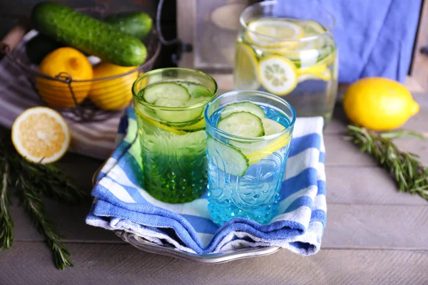 Fresh water with lemon and cucumber in glassware with napkin on wooden background — Stock Photo, Image