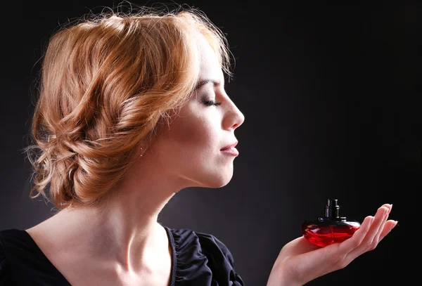 Mulher bonita com frasco de perfume no fundo preto — Fotografia de Stock