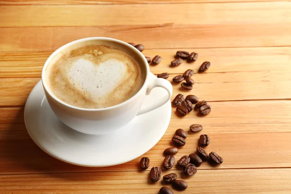 Taza de café latte arte con granos sobre fondo de madera — Foto de Stock