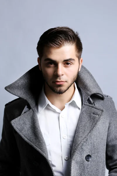 Jeune homme en manteau sur fond gris — Photo