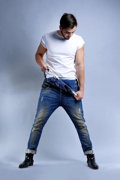 Muž v džínách kombinézy na šedém pozadí — Stock fotografie