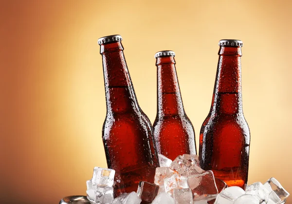 Glass bottles of beer in ice cubes on color background — Stock Photo, Image