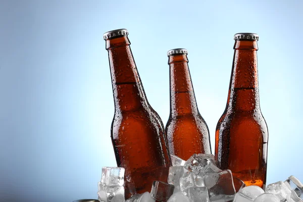 Glass bottles of beer in ice cubes on color background — Stock Photo, Image