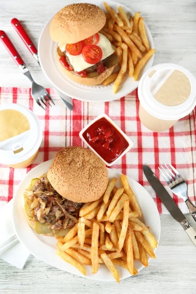 Tasty burger and french fries on plate, on wooden table background. Unhealthy food concept — Stock Photo, Image