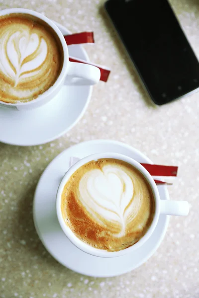 カフェでテーブルの上の泡の上の心とカプチーノのカップ — ストック写真