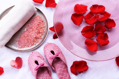 Spa kaseyle su, gül yaprakları, havlu ve terlik ışık arka plan üzerinde. Pedikür veya doğal kaplıca tedavisi kavramı