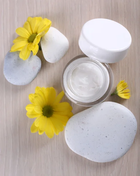 Crema cosmética con flores y piedras de spa sobre fondo de madera — Foto de Stock