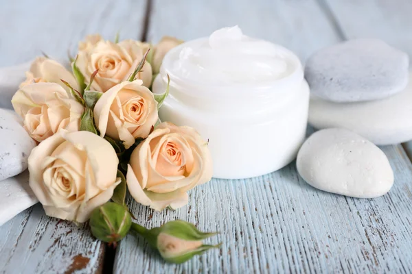 Crema cosmética con flores y piedras de spa sobre fondo de madera — Foto de Stock