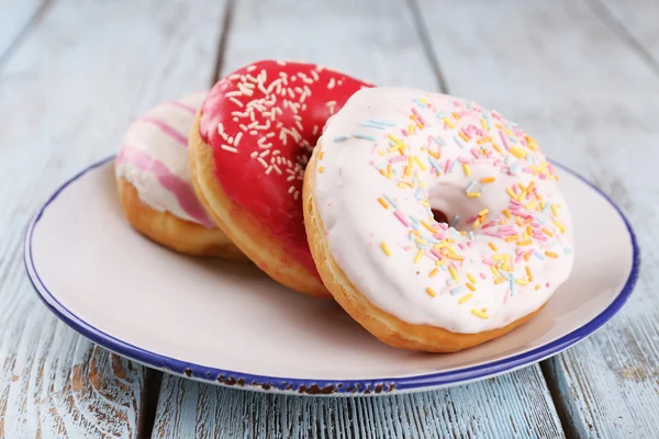 Delicious donuts with icing on plate on wooden background — Stock Photo, Image