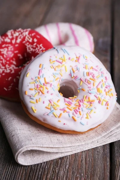 Köstliche Donuts mit Sahnehäubchen auf Serviette auf Holzgrund — Stockfoto