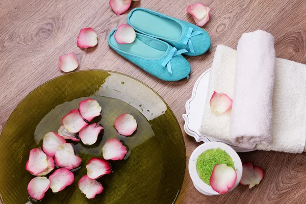 Spa bowl with water, rose petals, towel and slippers on light background. Concept of pedicure or natural spa treatment — Stock Photo, Image