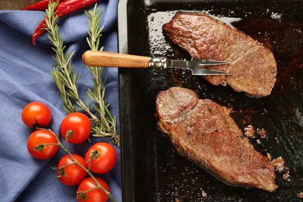 Composição com carne assada saborosa em panela, tomates e raminhos de alecrim em fundo de madeira — Fotografia de Stock