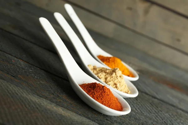 Different kinds of spices in spoons on wooden background — Stock Photo, Image