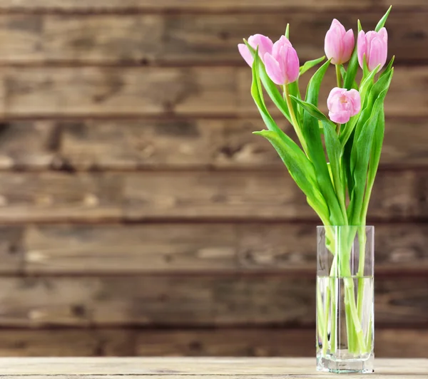 Beautiful pink tulips in vase on table on wooden background — Stock Photo, Image