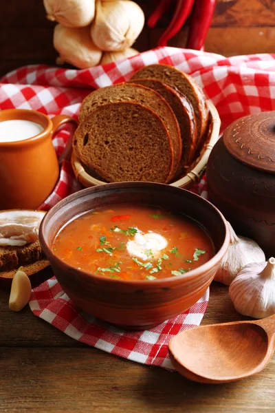 Oekraïense rode biet soep - Borsjt in kom en pot, op servet, op houten achtergrond — Stockfoto