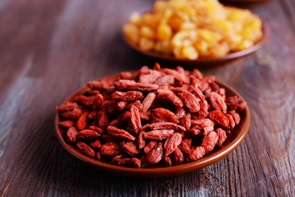 Pasas y Goji en pequeños platos sobre fondo rústico de mesa de madera —  Fotos de Stock