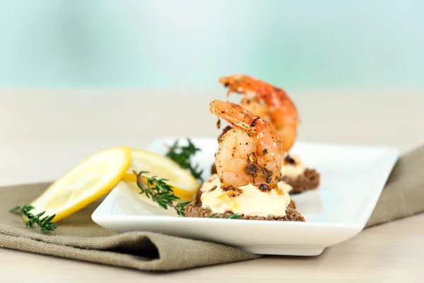 开胃菜烤面包片与虾和柠檬上浅色背景表格 — 图库照片