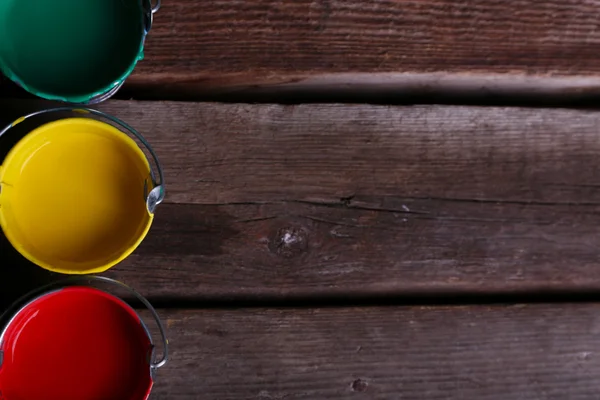 Metal buckets with colorful paint on wooden background — Stock Photo, Image