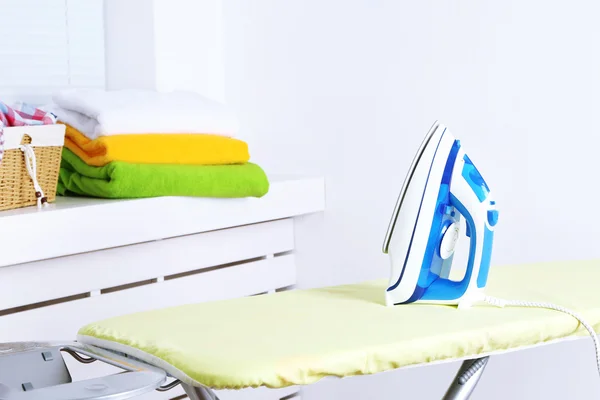 Iron on ironing board on light home interior background — Stock Photo, Image