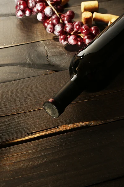 Стеклянная бутылка вина с пробками и виноградом на фоне деревянного стола — стоковое фото