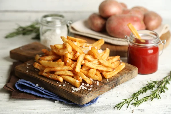 Batatas fritas saborosas na tábua de corte, no fundo da mesa de madeira — Fotografia de Stock
