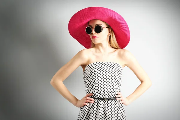 Экспрессивная молодая модель в розовой шляпе в солнечных очках на сером фоне — стоковое фото