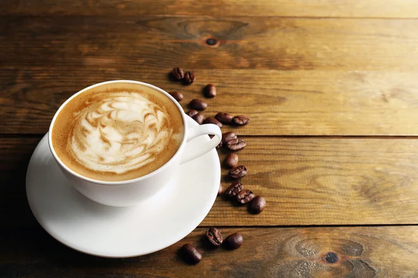 Cup of coffee latte art with grains on wooden background — Stock Photo, Image