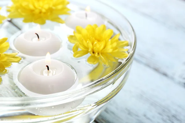 Bowl of spa water with flowers and candles on wooden table, closeup — Stock Photo, Image