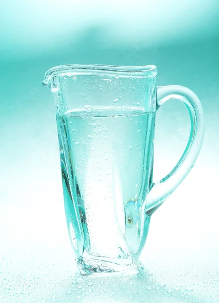 Glass pitcher of water on blue background — Stock Photo, Image