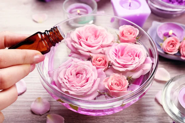 Female hand with bottle of essence and bowl of aroma spa water on wooden table, closeup — Stock Photo, Image