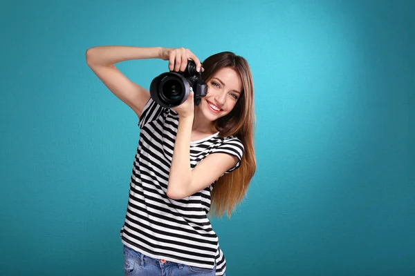 Young female photographer taking photos on blue background — Stock Photo, Image