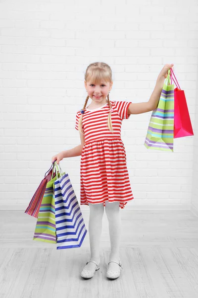 Vacker liten flicka med shoppingkassar i rum — Stockfoto