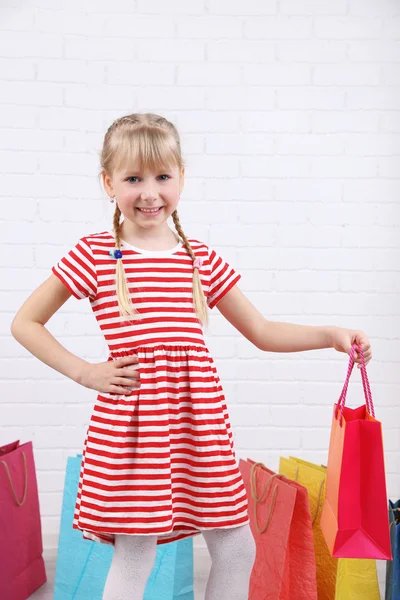 Schönes kleines Mädchen mit Einkaufstaschen im Zimmer — Stockfoto