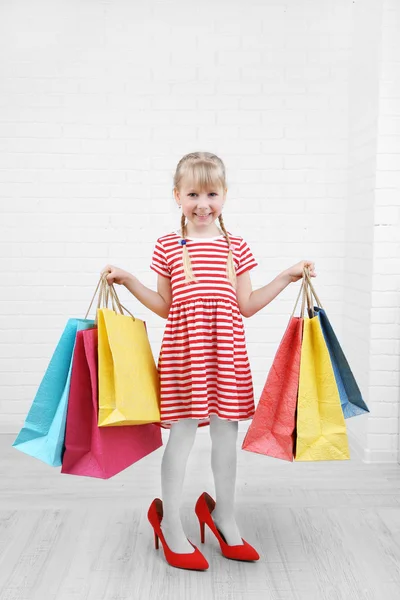 Belle petite fille dans les chaussures de maman avec des sacs à provisions dans la chambre — Photo