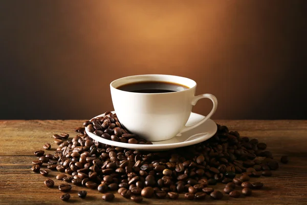 Tasse de café avec des grains sur table en bois sur fond sombre — Photo